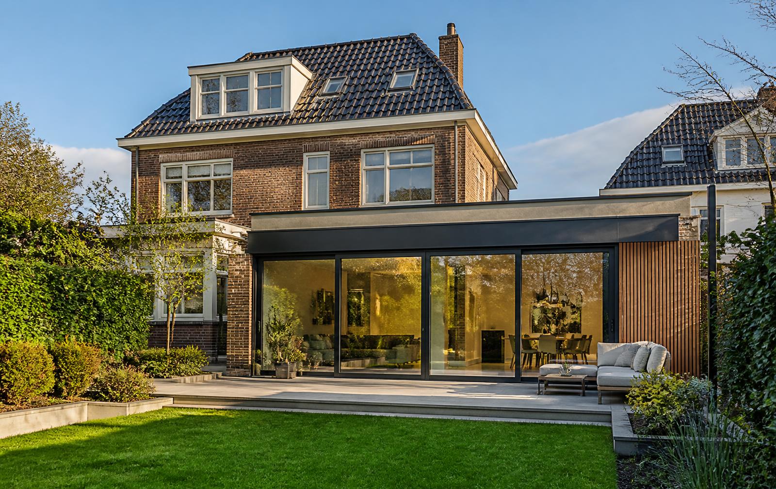 Achteruitbouw van een jaren '30 woning, van buiten uit de tuin gezien met schuifpui en plat dak